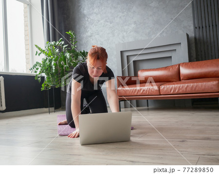 Woman on yoga mat front of laptop looking into 77289850