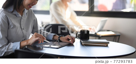 Cropped shot of happy female employee working on digital tablet while sitting with her colleague in office. 77293783