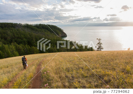 traveler with backpack, tourist going on a country road in the steppe, towards the forest and water 77294062
