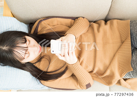 ソファに寝転がってスマホを持つ女性 77297436