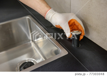 A plumber is setting the start button for the waste shredder on the kitchen sink. 77303048