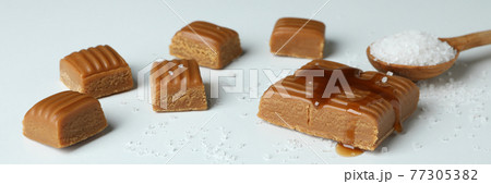 Caramel pieces and spoon of salt on white background 77305382