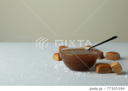 Salted caramel pieces and bowl of sauce on light gray table 77305384
