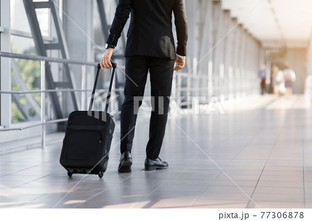 Cropped of businessman walking by airport with suitcase, back view Cropped of businessman walking by airport with suitcase, back view 77306878