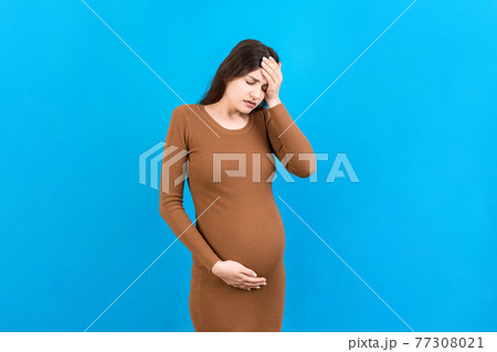 Beautiful young pregnant woman feeling head ache on colored background isolated. Stressed pregnant woman or mother problems 77308021