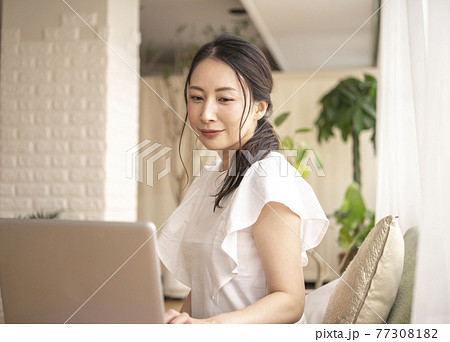 自宅で座りながらパソコンを操作する女性 77308182