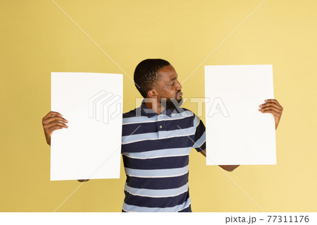 Happy African man with blank sheets of paper isolated over yellow studio background 77311176