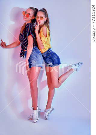 Two female teenagers in sunglasses and summer clothes posing in studio on white background Two female teenagers in sunglasses and summer clothes posing in studio on white background 77311824