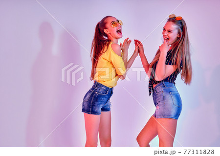 Two female teenagers in sunglasses and summer clothes posing in studio on white background Two female teenagers in sunglasses and summer clothes posing in studio on white background 77311828