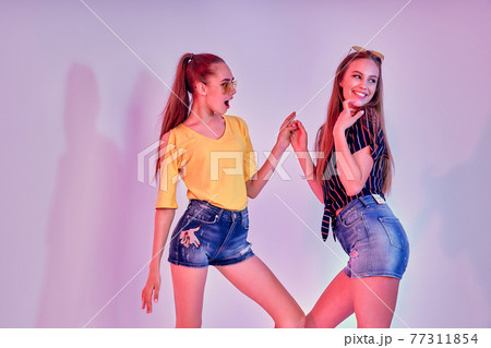 Two female teenagers in sunglasses and summer clothes posing in studio on white background 77311854
