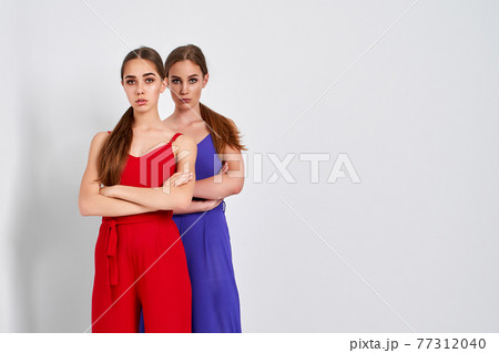 Two girls standing in studio in elegant colorful overalls on white background Two girls standing in studio in elegant colorful overalls on white background 77312040
