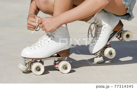 Close-up detail of skater's hands tying the laces of a roller skate 77314345