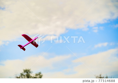A pink plastic children's airplane toy flying in blue sky surrounded with white clouds 77314688