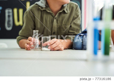 Boy hands holding flask and vessel while sitting at the desk Boy hands holding flask and vessel while sitting at the desk 77316186