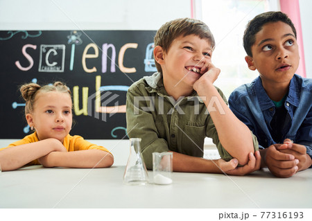 Group of multiracial kids sitting at the desk and listening their teacher Group of multiracial kids sitting at the desk and listening their teacher 77316193