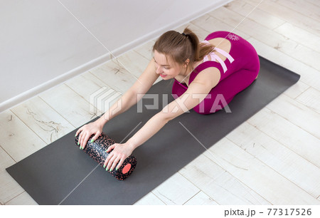 Beautiful woman pilates instructor stretching and warming up using foam roller, working out, wearing pink sportswear, close up. Sport and healthy active lifestyle concept. 77317526