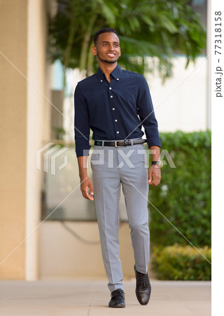 Full length shot of handsome African businessman outdoors walking and smiling Full length shot of handsome African businessman outdoors walking and smiling 77318158