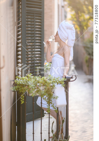 young girl after shower with a glass of wine. girl took a shower and stands on a balcony drinks white wine from a glass 77318800