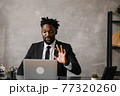 Confident young african man look at webcam conference video calling in office, happy mixed race entrepreneur talking doing online video chat job interview sit at desk 77320260