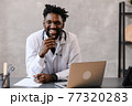 Handsome contented African American doctor working on a laptop. telemedicine 77320283