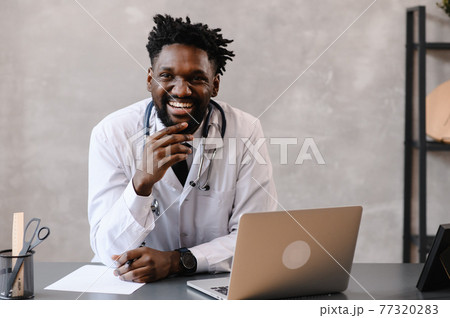 Handsome contented African American doctor working on a laptop. telemedicine 77320283