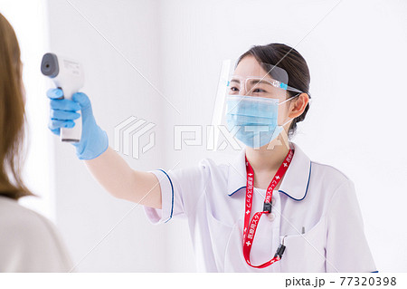 非接触体温計で体温測定をする看護師 77320398