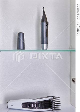Household appliances for home haircuts such as nose, eyebrow and ear trimmer and head hair clipper are stored in bathroom wall cabinet. Household appliances for home haircuts such as nose, eyebrow and ear trimmer and head hair clipper are stored in bathroom wall cabinet. 77320677