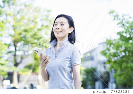 屋外でスマートフォンを操作する中年女性 77322182
