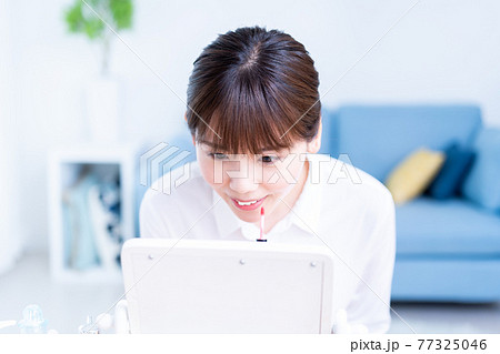 リビングで鏡を見ながら口紅を塗る若い女性 77325046