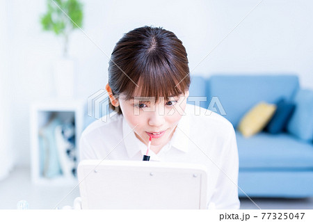 リビングで鏡を見ながら口紅を塗る若い女性 77325047