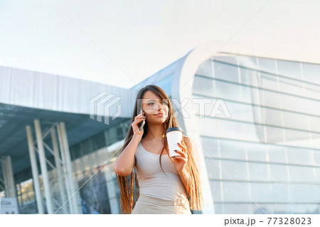 Happy Woman Calling On Phone Standing Near Office. Portrait Of Beautiful Smiling Female Holding Cup Of Coffee In Hand, Talking On Phone Outdoors. 77328023