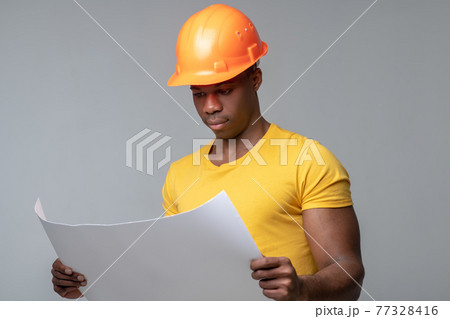 Serious man in helmet considering blueprint drawing Serious man in helmet considering blueprint drawing 77328416