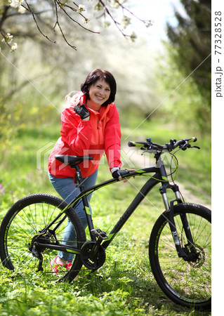 Beautiful woman on a bike in a blooming spring garden. Beautiful mature woman posing for the camera in a blooming spring garden. Beautiful woman on a bike in a blooming spring garden. Beautiful mature woman posing for the camera in a blooming spring garden. 77328528