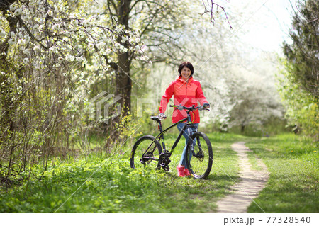 Beautiful woman on a bike in a blooming spring garden. Beautiful mature woman posing for the camera in a blooming spring garden. 77328540