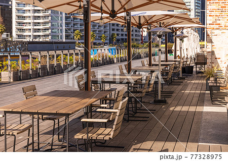 レストランの前のテラスにある日除けパラソルとテーブル 77328975