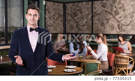 Elegant waiter with welcome gesture in restaurant hall Elegant waiter with welcome gesture in restaurant hall 77330315