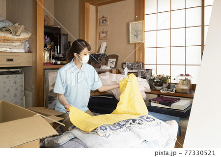 マスクをして散らかった部屋の片付けをする女性作業員 77330521