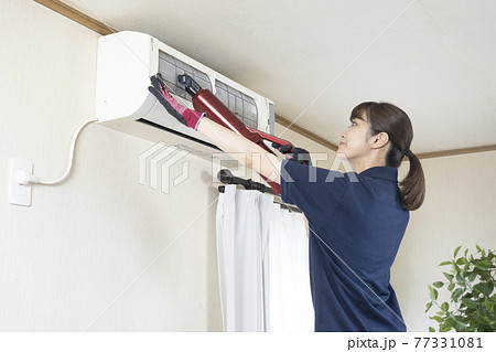 掃除機でエアコンの清掃をするハウスクリーニングの女性作業員 77331081