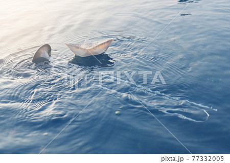 wind instrument pipe lies in the water, in the sea or ocean, next to a paper boat of music, a concept 77332005