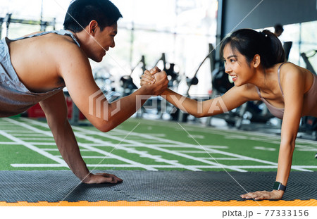 Healthy smiling couple of man and woman giving high five to each other while pushing up in the fitness gym. Asian sporty people working out together Healthy smiling couple of man and woman giving high five to each other while pushing up in the fitness gym. Asian sporty people working out together 77333156