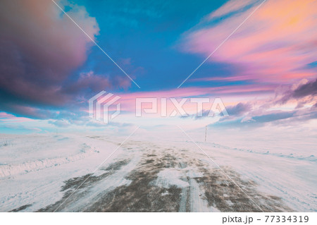 Snow-covered Open Slippy Road During A Snowstorm Blizzard In Winter. Altered Colorful Sunset Sunrise Sky. Dangerous Motion Snow-covered Open Slippy Road During A Snowstorm Blizzard In Winter. Altered Colorful Sunset Sunrise Sky. Dangerous Motion 77334319