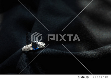 white gold with blue sapphire and diamond ring isolated on black fabric background white gold with blue sapphire and diamond ring isolated on black fabric background 77334746