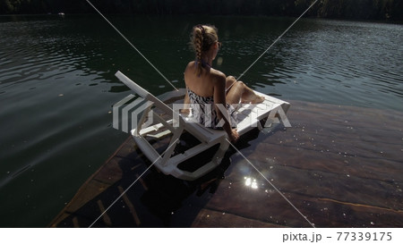 Woman lie on a sunbed in sunglasses and a boho silk shawl. Girl rest on a flood wood underwater pier. The pavement is covered with water in the lake. Woman lie on a sunbed in sunglasses and a boho silk shawl. Girl rest on a flood wood underwater pier. The pavement is covered with water in the lake. 77339175