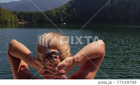 Woman sit on a sunbed in sunglasses and swimming suit. Girl rest on a flood wood underwater pier. The pavement is covered with water in lake. 77339799