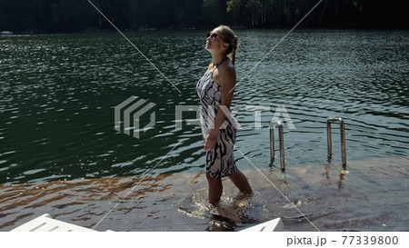 Woman lie on a sunbed in sunglasses and a boho silk shawl. Girl rest on a flood wood underwater pier. The pavement is covered with water in the lake. 77339800