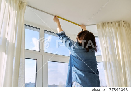 Service for sewing and hanging curtains. Woman with tape measure measuring window Service for sewing and hanging curtains. Woman with tape measure measuring window 77345048