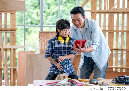 Asian man hold and show tablet to boy and they look happy during carpentering work in their house. Asian man hold and show tablet to boy and they look happy during carpentering work in their house. 77347399