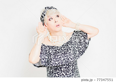 白背景の前に立って、聞き耳を立てるドラァグクイーン 77347551