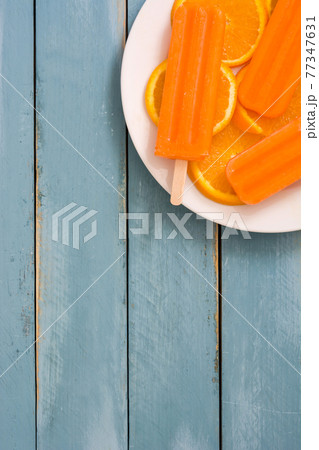 Orange popsicles on blue wooden background Orange popsicles on blue wooden background 77347631