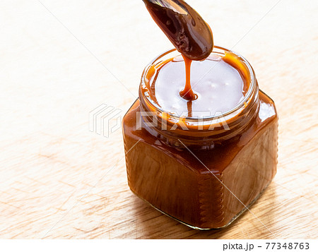 cooking salted butter caramel sauce at home kitchen - homemade smooth salty caramel dessert in open glass jar on wooden board close up cooking salted butter caramel sauce at home kitchen - homemade smooth salty caramel dessert in open glass jar on wooden board close up 77348763